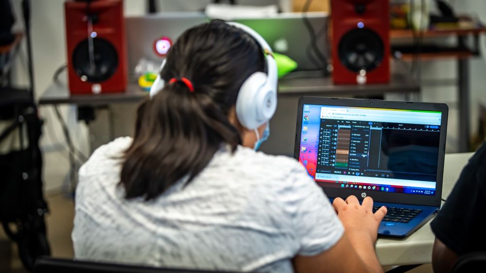 A student wearing headphones creates music on a laptop in an LTBB lab.