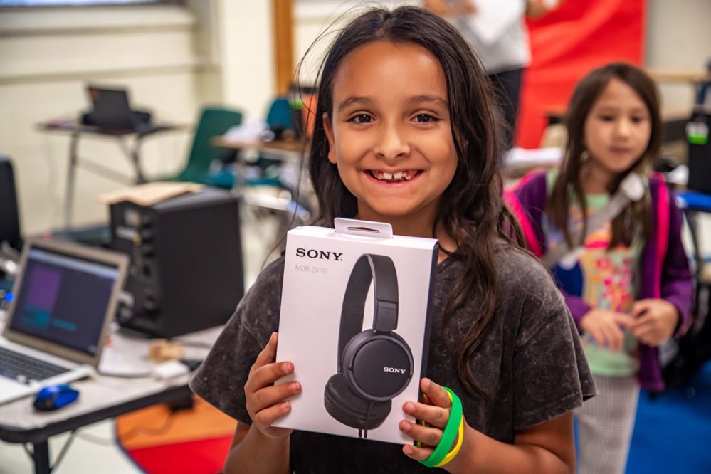 A young LTBB participant smiles while holding a new pair of headphones in a music lab.