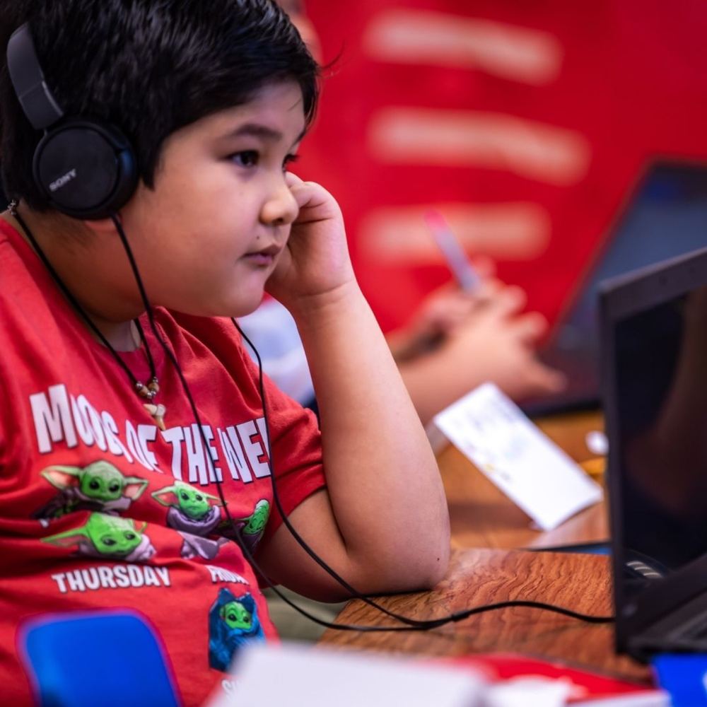 A young student listens closely through headphones while working at a computer.