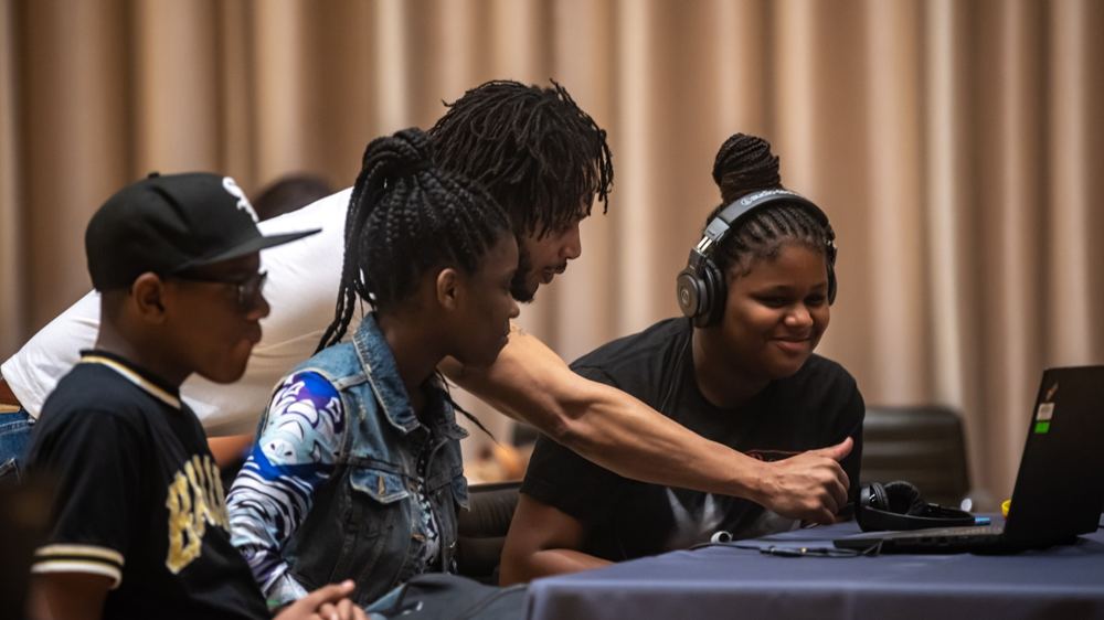 Young people and an LTBB mentor gather around a laptop during a music technology session.