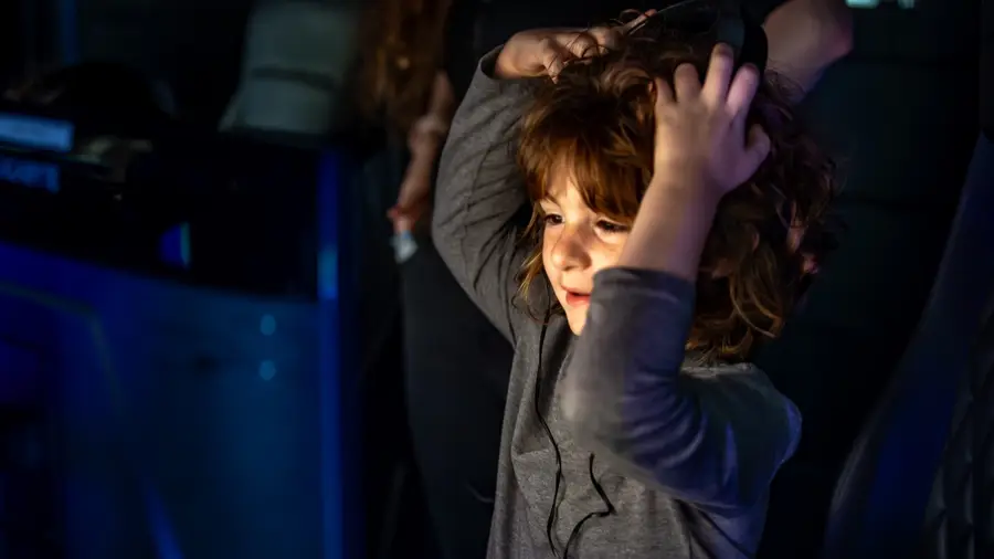 A young student listens closely through studio headphones in a dark music lab.