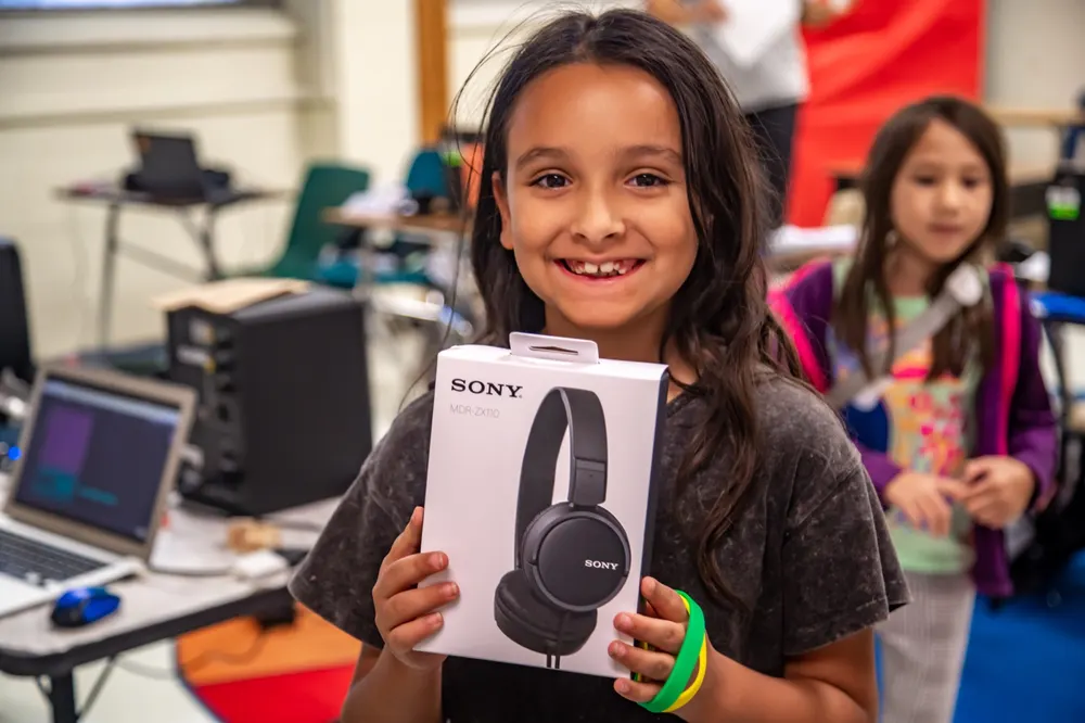 A young LTBB participant smiles while holding a new pair of headphones in a music lab.