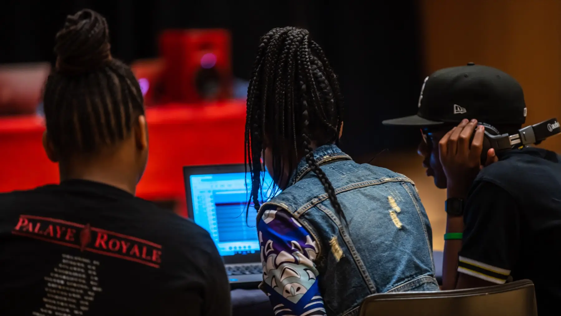 Three students collaborate on music production around a laptop.