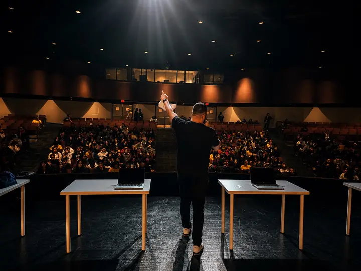 An LTBB presenter leads a live assembly from the stage as students respond in the auditorium.