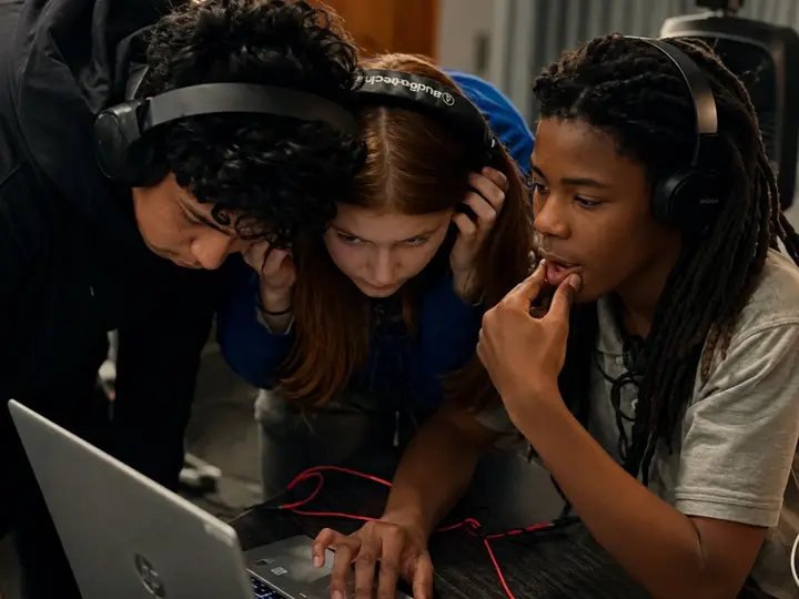 Three students wearing headphones build a beat together at an LTBB live experience.