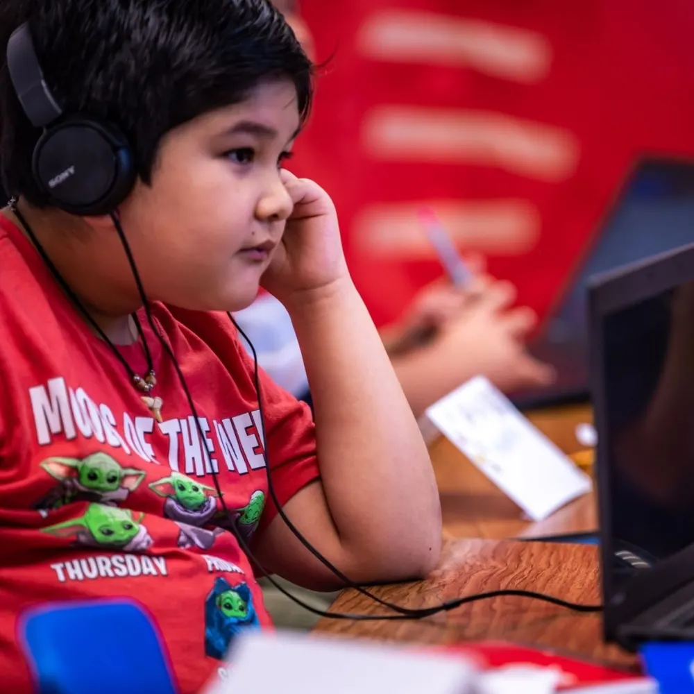 A young student listens closely through headphones while working at a computer.