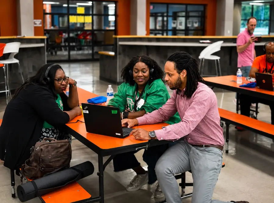Three adult participants collaborate around a laptop during an LTBB workshop at Lancaster ISD.